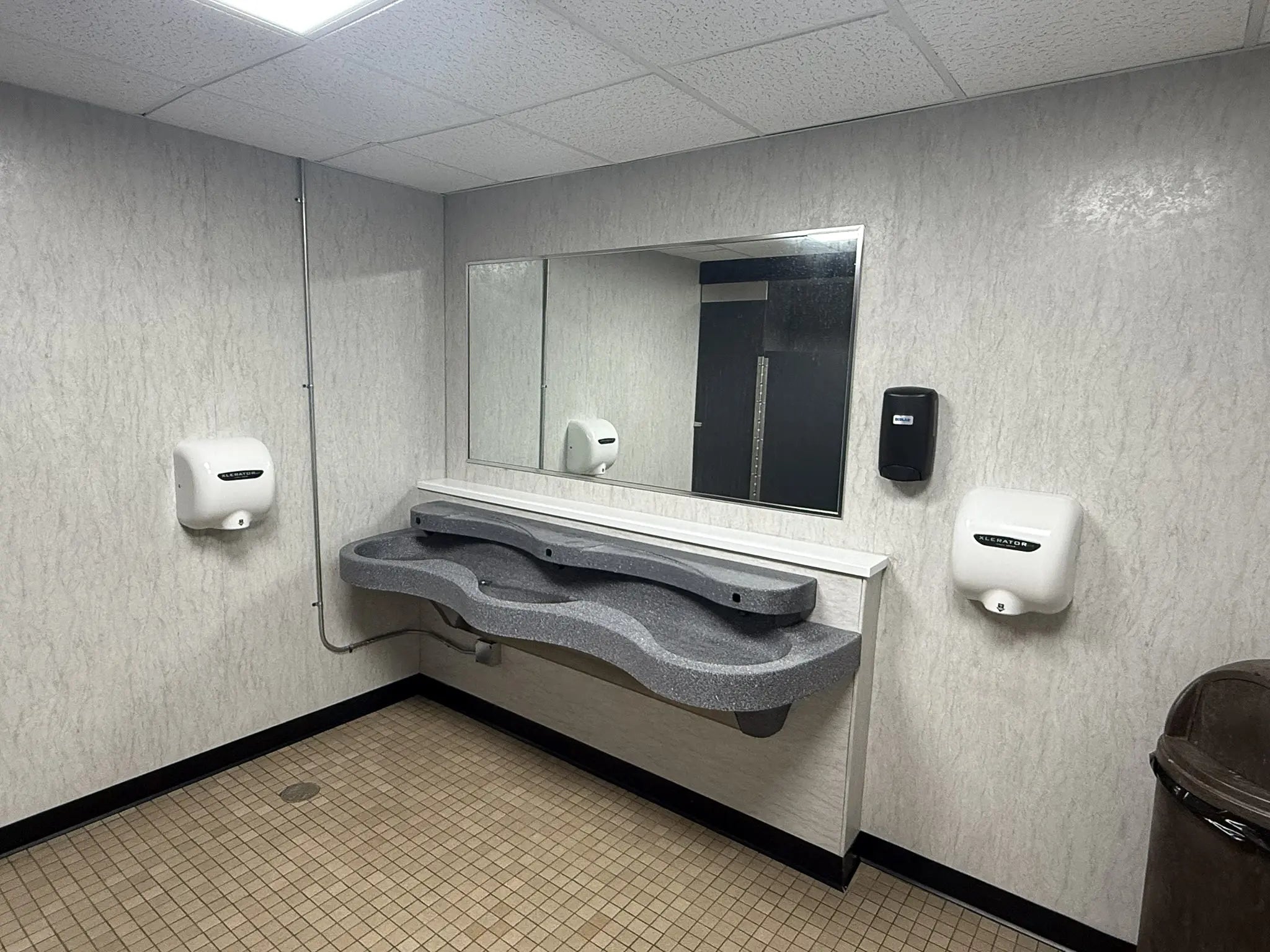 Bathroom stall with sink, mirror, and hand dryers on a textured wall.