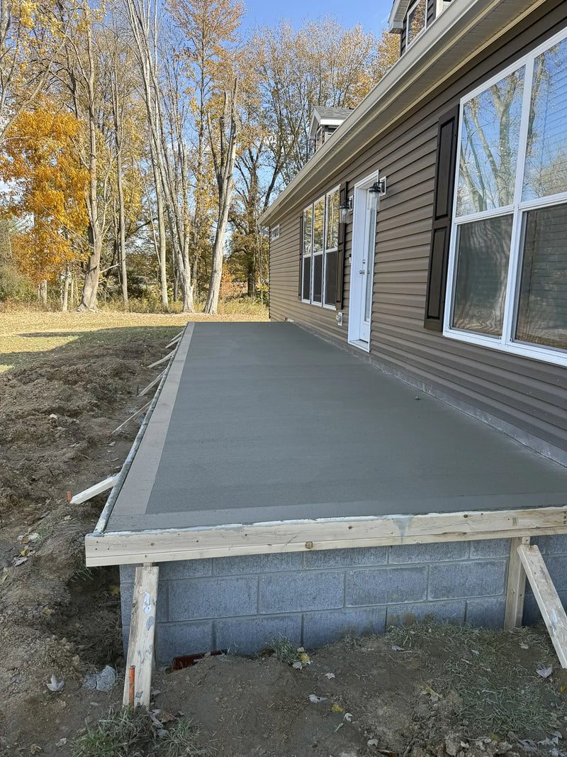 Newly poured concrete slab in front of a house with trees in the background