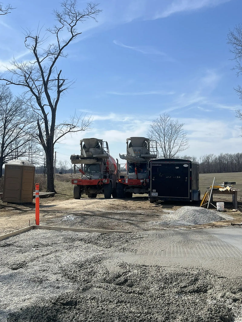 Two trucks with construction equipment on a concrete surface under a clear blue sky.