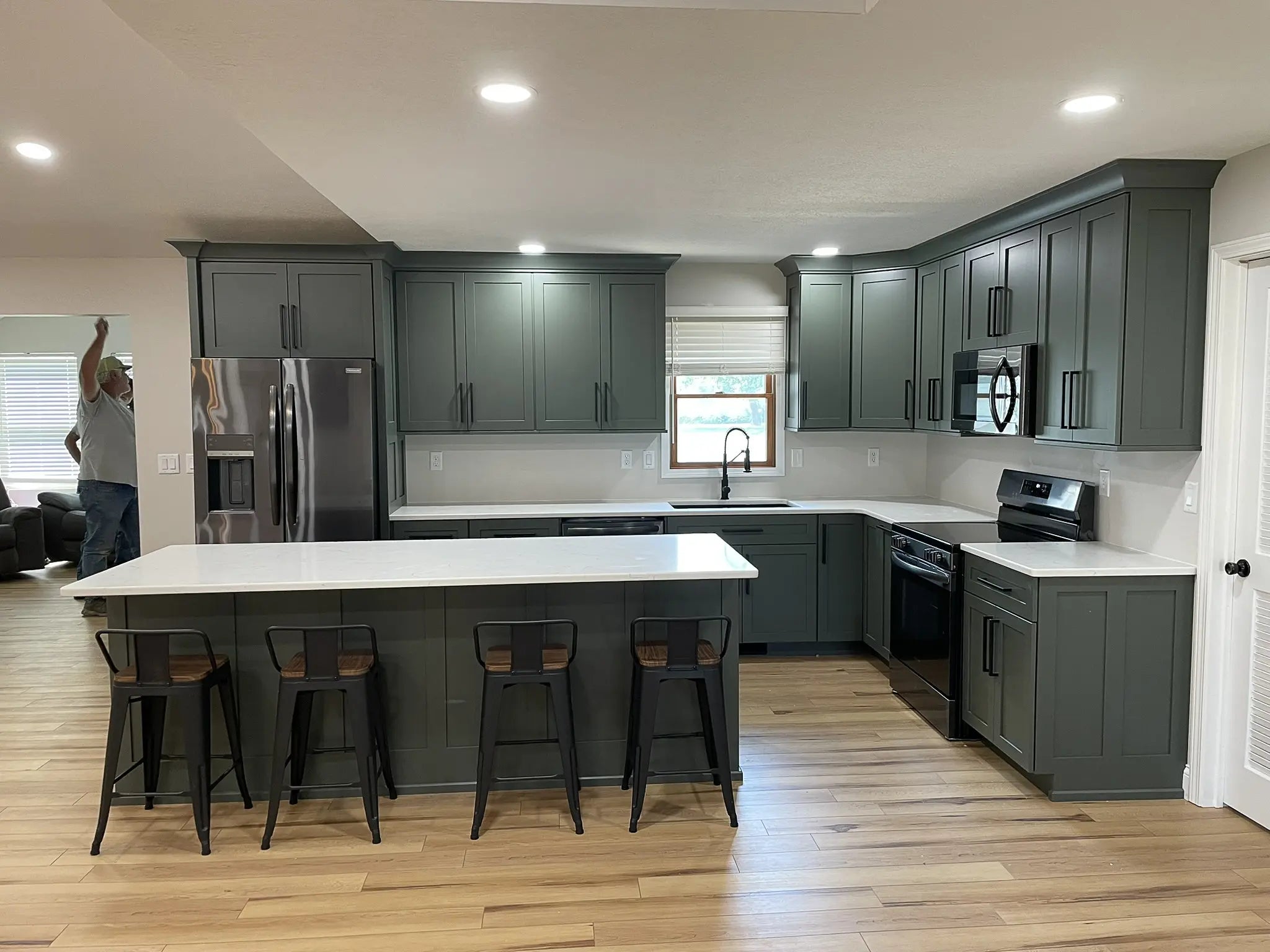 Modern kitchen with green cabinets, white countertops, and stainless steel appliances.