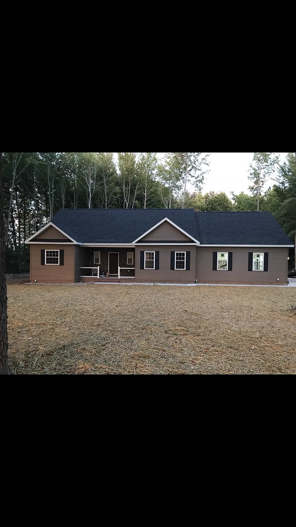 Two-story house with a gray roof and brown exterior in a wooded area.