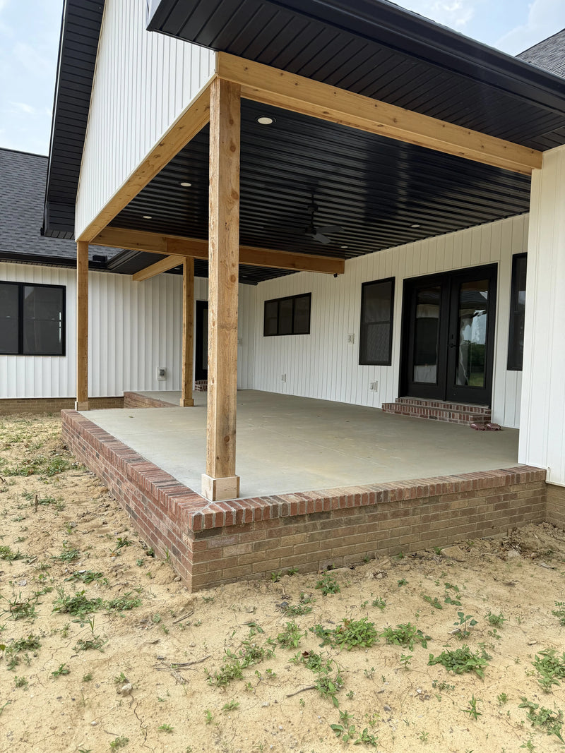 Wooden deck structure in front of a house with a dirt area and grass patches.