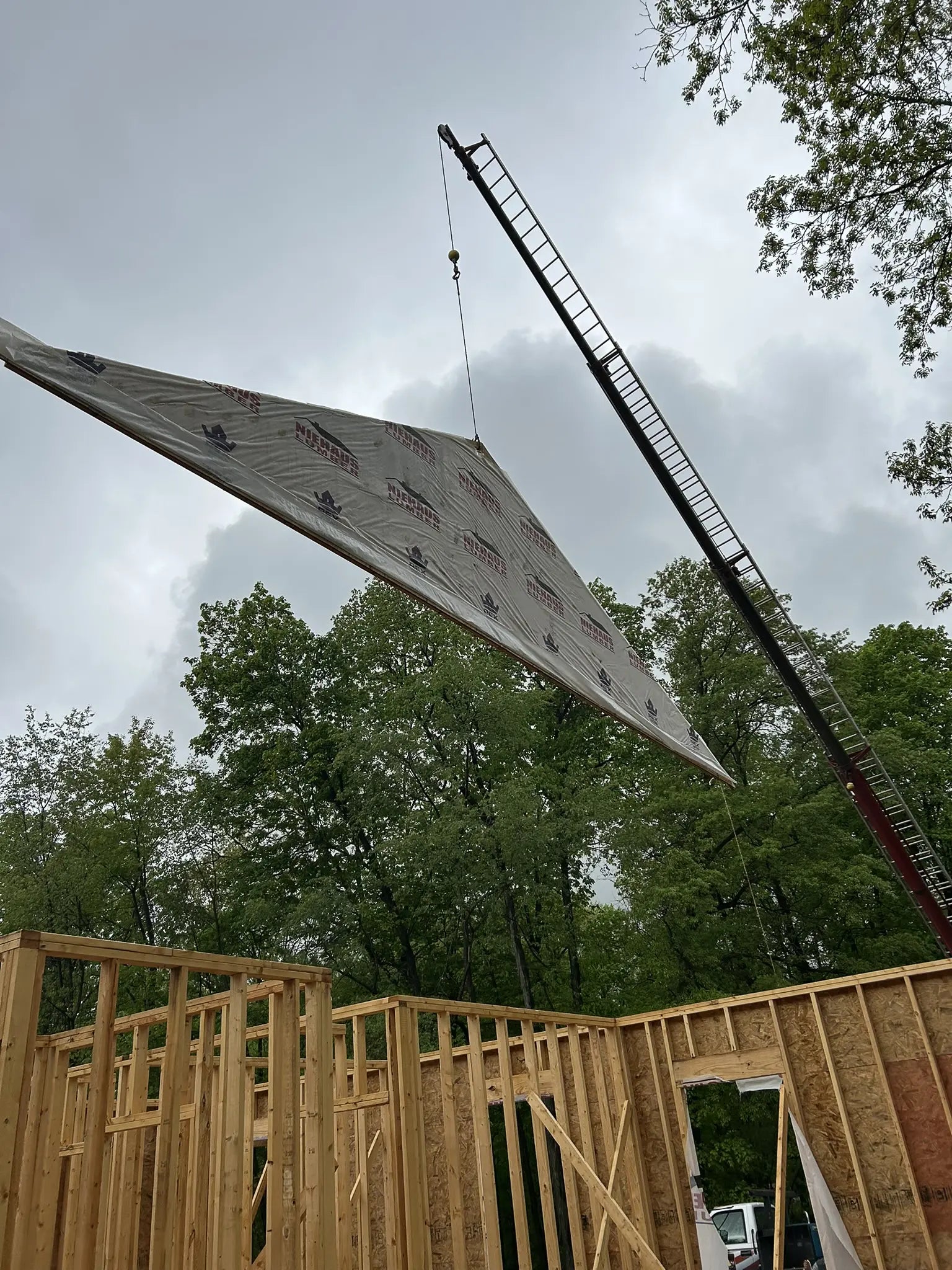 Construction site with a crane lifting a large sheet of material against a cloudy sky.
