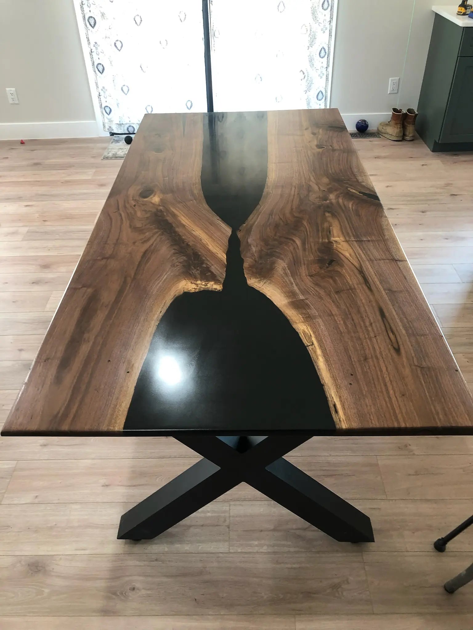 Wooden resin dining table with black metal legs on a wooden floor.