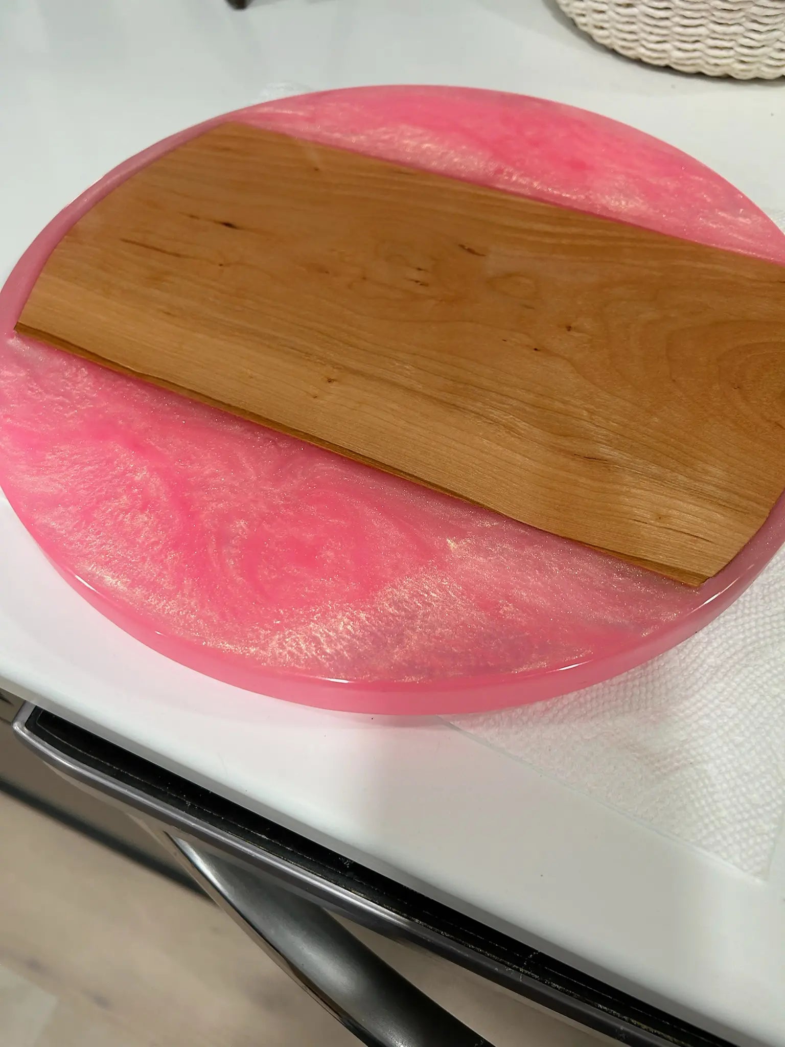 Pink resin circular serving tray with a wooden top on a white surface