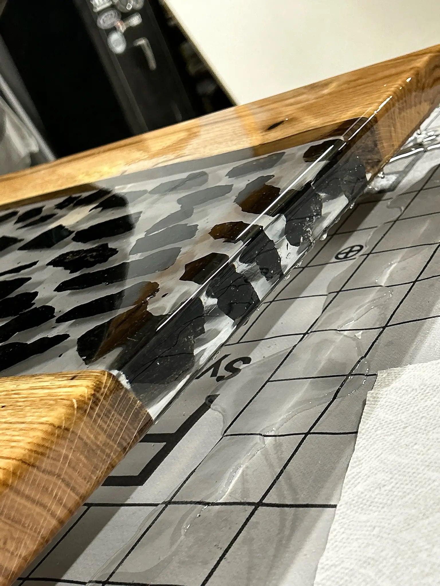 close up of wooden epoxy table with coal chunks embedded in the resin sitting on top of grid
